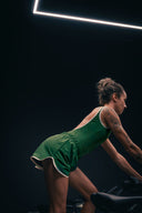 Body Tennis Club vert porté avec un short assorti, vu de trois quarts dos sur un vélo de salle