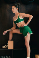 Brassière de sport Tennis Club verte à bordures crème, portée avec le short assorti, une jambe surélevée