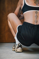 Short de sport The All Black noir à bordures claires, détail de dos en position accroupie