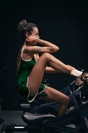 Body Tennis Club vert vu de profil, porté avec un short en position assise sur un vélo de salle