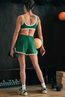 Brassière Tennis Club verte portée debout de dos, avec bretelles et encolure soulignées de crème.